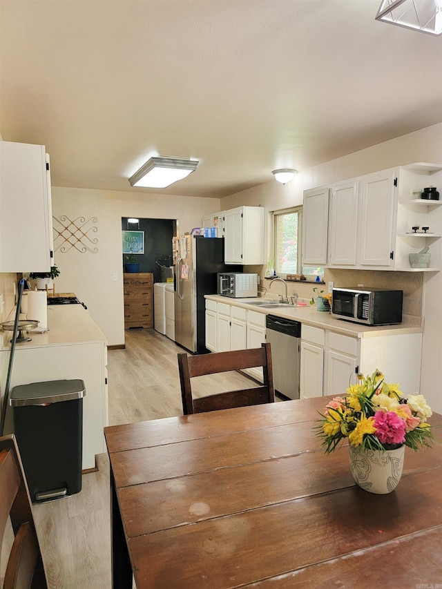1209 Cole Ave, Mena, AR 71953 - kitchen with stainless steel appliances, washer and dryer, light wood-type flooring, open shelves, and white cabinetry