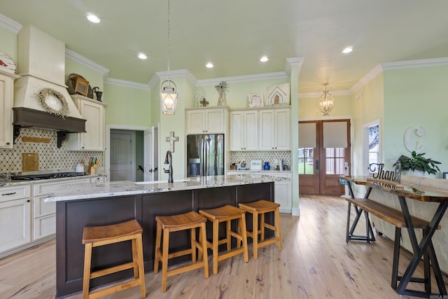 13518 Pikes Peak Pl, Rogers, AR 72756 - kitchen featuring stainless steel fridge, decorative backsplash, light stone counters, an island with sink, and a kitchen bar