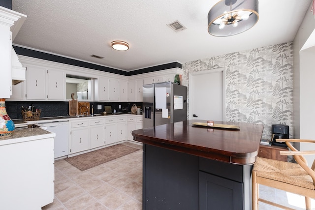 kitchen featuring stainless steel fridge with ice dispenser, wallpapered walls, dishwasher, white cabinets, and backsplash