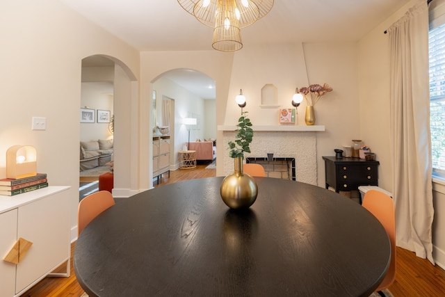 dining space with arched walkways, wood finished floors, plenty of natural light, and a fireplace