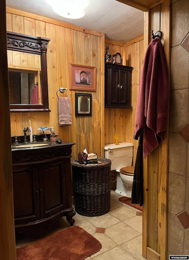 bathroom featuring tile flooring, wooden walls, a textured ceiling, toilet, and vanity