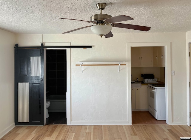 interior space with a barn door, ceiling fan, light hardwood / wood-style flooring, and electric stove