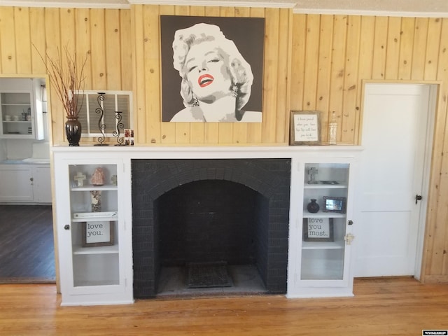 unfurnished living room featuring wood walls, light wood-type flooring, and a brick fireplace