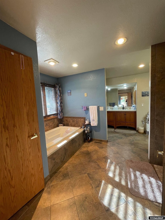 bathroom with a textured ceiling, a relaxing tiled bath, tile floors, and vanity