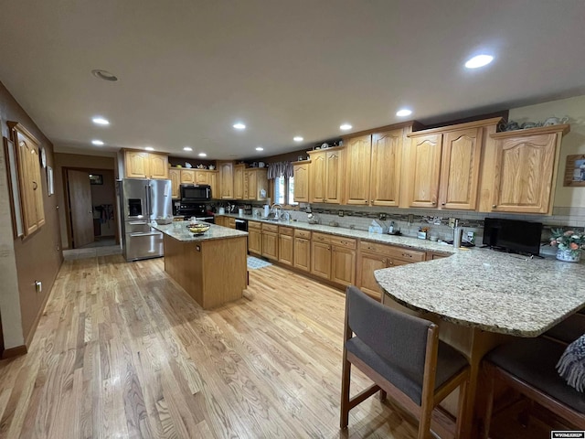 kitchen with stainless steel fridge with ice dispenser, a breakfast bar area, light hardwood / wood-style floors, range, and a center island