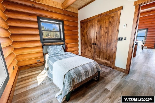 bedroom with hardwood / wood-style floors, beam ceiling, and a closet