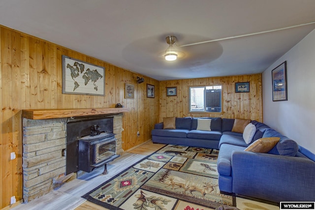 living room with ceiling fan, a wood stove, light wood-type flooring, and wooden walls