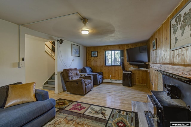 living room with a baseboard radiator, ceiling fan, wood walls, and light wood-type flooring