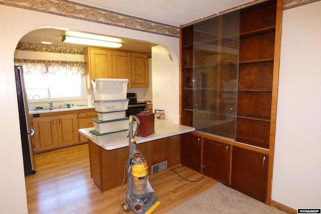 kitchen featuring stainless steel fridge, sink, kitchen peninsula, and light hardwood / wood-style floors