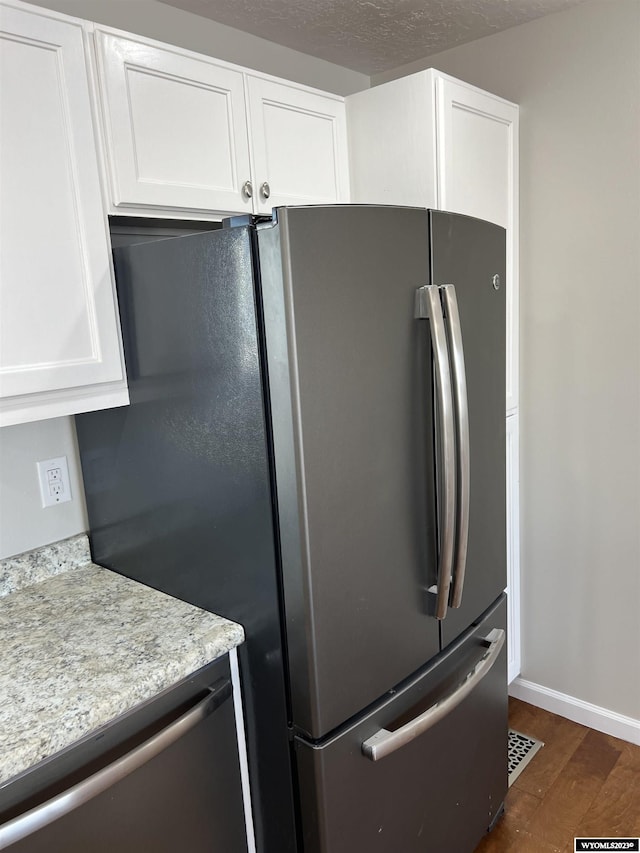 kitchen featuring white cabinets, appliances with stainless steel finishes, light stone counters, and dark wood-type flooring