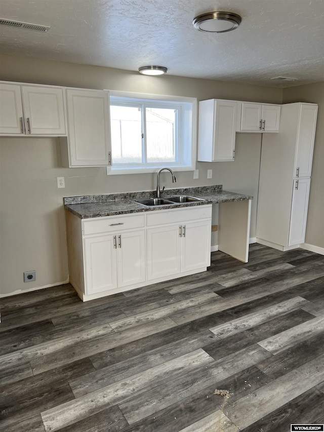 kitchen with a textured ceiling, dark wood-type flooring, sink, dark stone countertops, and white cabinets