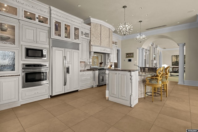 kitchen featuring hanging light fixtures, built in appliances, ornamental molding, light tile patterned flooring, and ornate columns