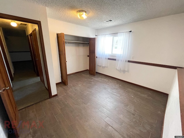 unfurnished bedroom with baseboards, visible vents, dark wood-style floors, a textured ceiling, and a closet