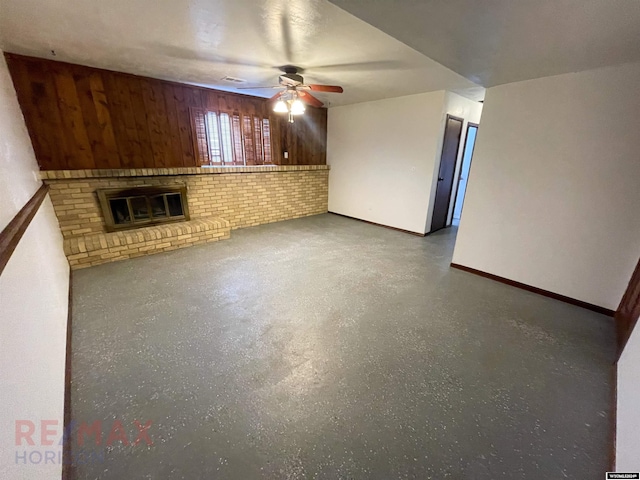 unfurnished living room featuring ceiling fan, wood walls, a fireplace, and baseboards