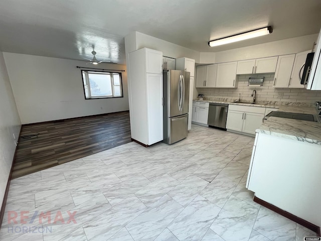 kitchen featuring decorative backsplash, white cabinets, light stone counters, appliances with stainless steel finishes, and a sink