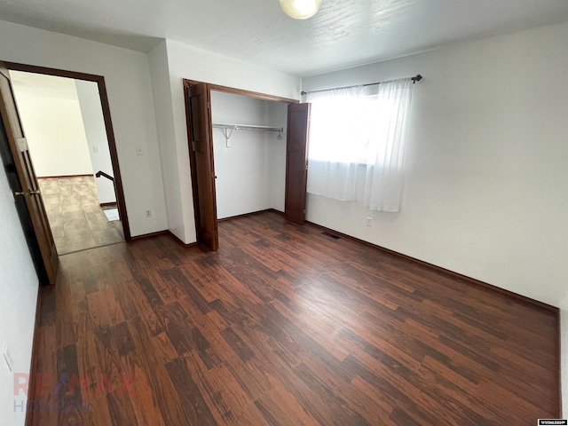 unfurnished bedroom featuring dark wood-style floors, baseboards, visible vents, and a closet