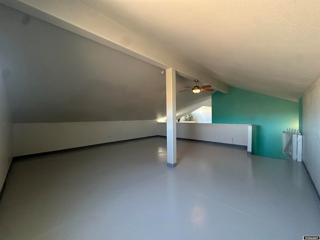 additional living space with lofted ceiling with beams, ceiling fan, concrete flooring, and a textured ceiling