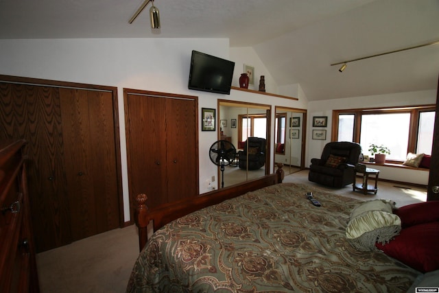 bedroom featuring lofted ceiling, light colored carpet, rail lighting, and multiple closets