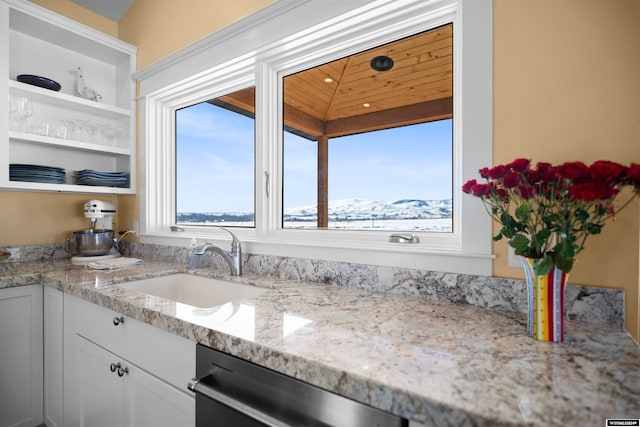 kitchen with stainless steel dishwasher, light stone counters, vaulted ceiling, sink, and white cabinetry