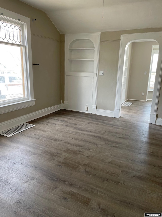 empty room featuring plenty of natural light, built in features, and dark hardwood / wood-style flooring