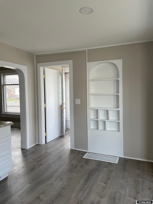 spare room with built in shelves and dark wood-type flooring