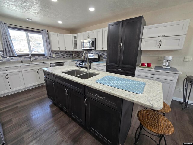 kitchen featuring appliances with stainless steel finishes, tasteful backsplash, sink, a kitchen island with sink, and dark hardwood / wood-style floors