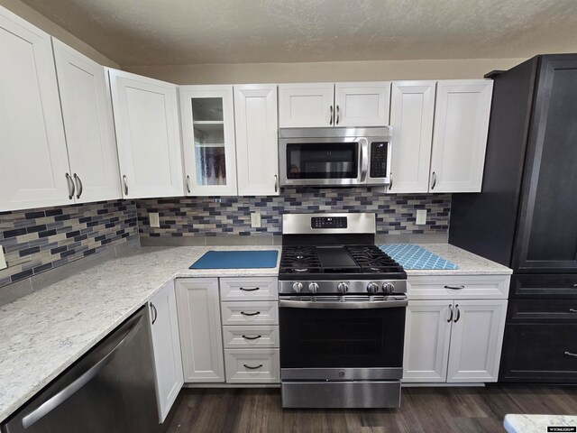 kitchen with white cabinets, dark hardwood / wood-style floors, stainless steel appliances, light stone countertops, and backsplash