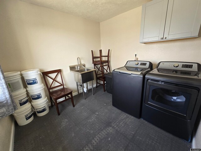 laundry room featuring dark tile floors, washing machine and clothes dryer, a textured ceiling, and cabinets