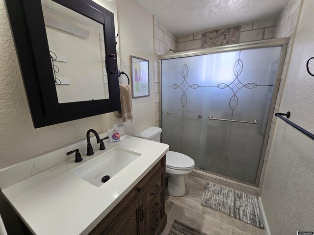 bathroom featuring tile floors, a shower with door, a textured ceiling, toilet, and vanity