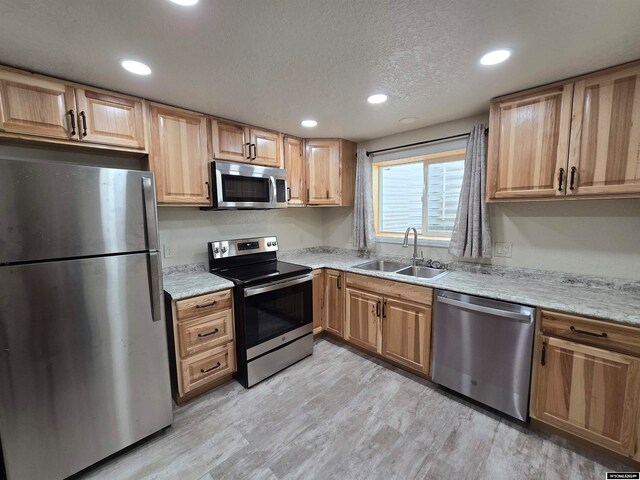 kitchen featuring sink, light stone counters, stainless steel appliances, a textured ceiling, and light wood-type flooring