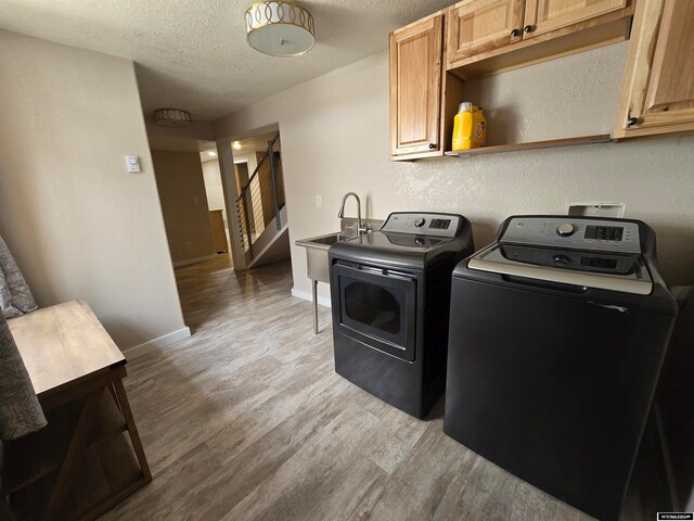 laundry area featuring cabinets, independent washer and dryer, sink, a textured ceiling, and light wood-type flooring