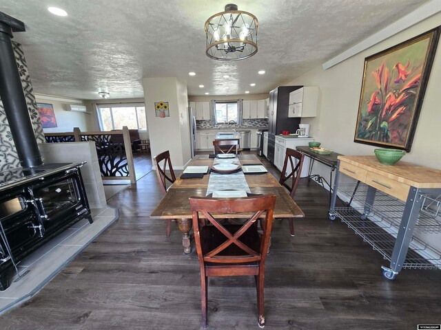 dining area with an inviting chandelier, a textured ceiling, dark hardwood / wood-style floors, and a wood stove