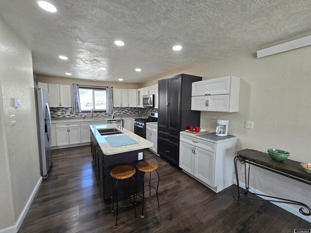 kitchen featuring stainless steel appliances, white cabinets, a kitchen island with sink, and dark wood-type flooring