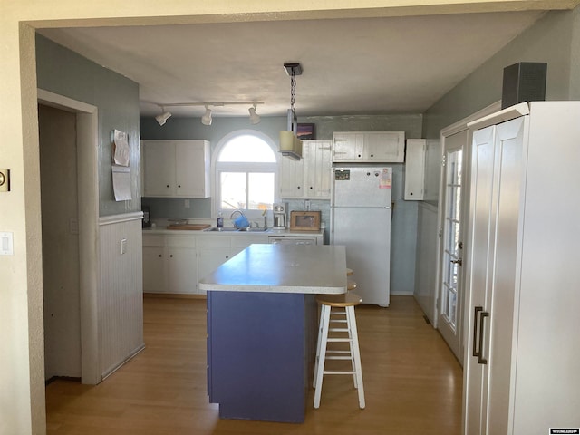 kitchen featuring white refrigerator, white cabinetry, a kitchen bar, and light wood-type flooring