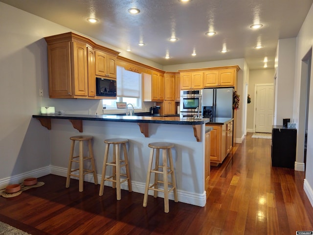 kitchen with appliances with stainless steel finishes, a breakfast bar, sink, kitchen peninsula, and dark wood-type flooring