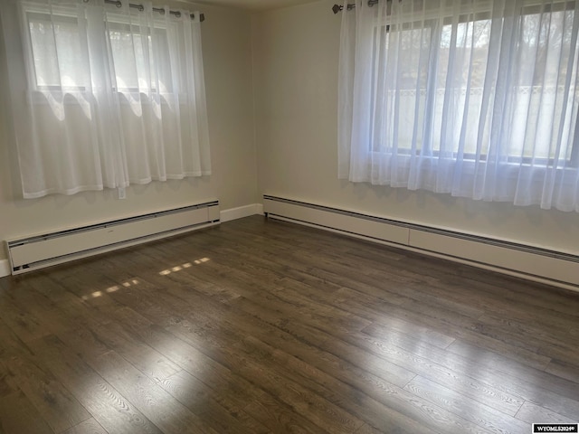 empty room featuring dark hardwood / wood-style floors, a baseboard radiator, and a wealth of natural light