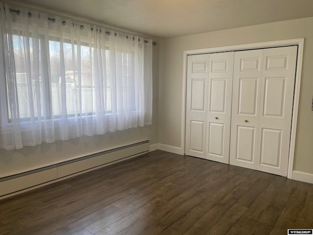 unfurnished bedroom featuring a baseboard heating unit, dark wood-type flooring, and a closet