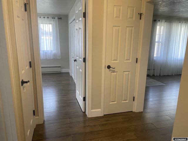 hallway featuring a textured ceiling, dark wood-type flooring, and a baseboard heating unit