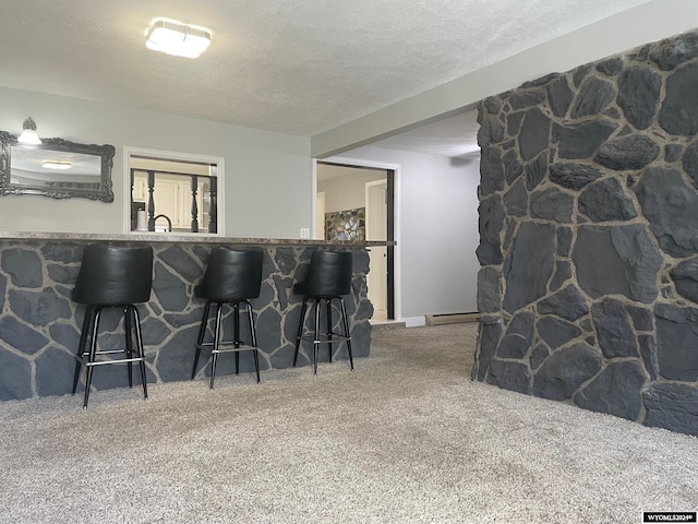 kitchen featuring baseboard heating, carpet flooring, kitchen peninsula, a breakfast bar area, and a textured ceiling