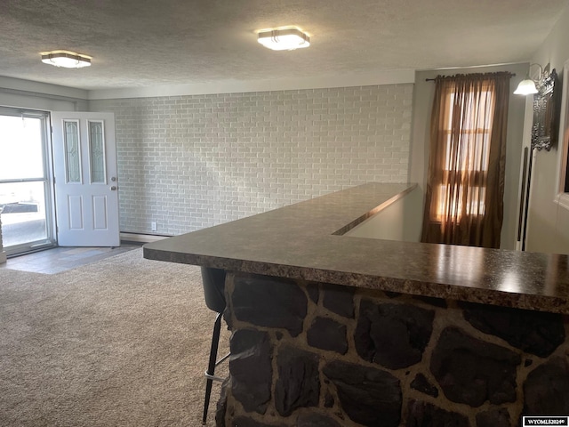 kitchen with a textured ceiling, carpet floors, and a kitchen bar