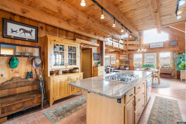 kitchen featuring light tile flooring, track lighting, beam ceiling, wooden walls, and a center island