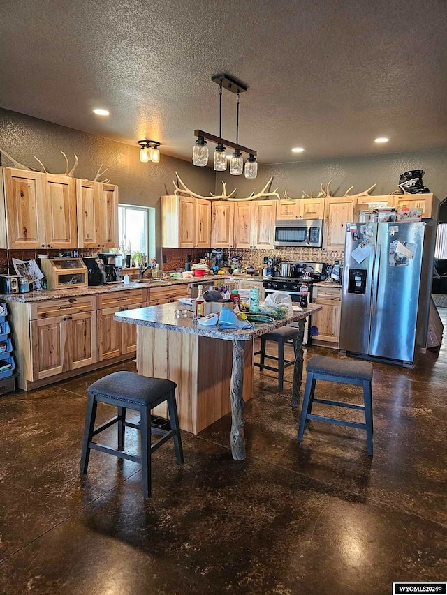 kitchen featuring appliances with stainless steel finishes, a textured ceiling, sink, pendant lighting, and a center island