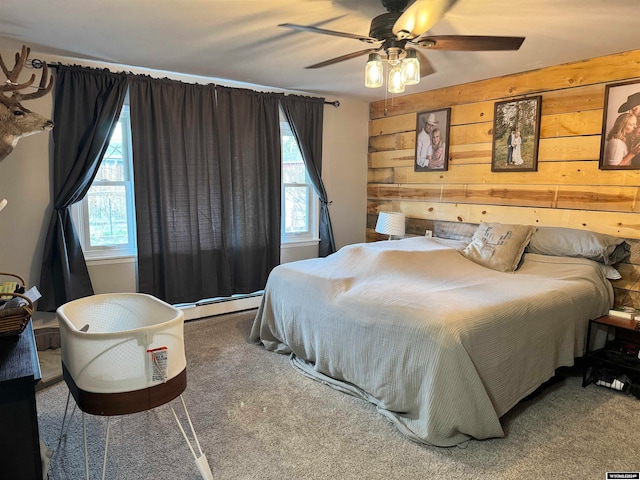 carpeted bedroom with wooden walls, a baseboard heating unit, ceiling fan, and multiple windows