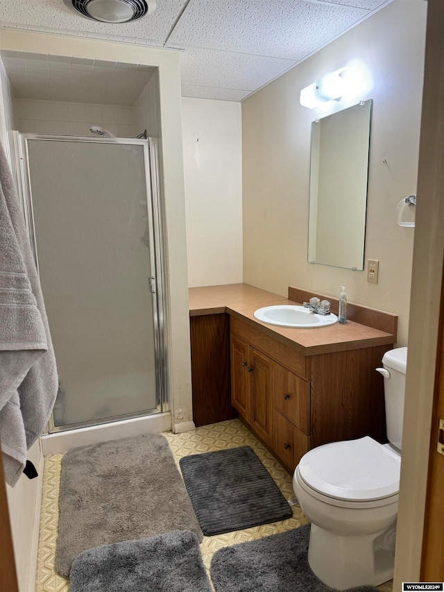 bathroom with vanity, a shower with shower door, tile flooring, toilet, and a paneled ceiling