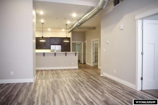 kitchen with a kitchen bar, decorative light fixtures, wood-type flooring, stainless steel fridge, and a center island