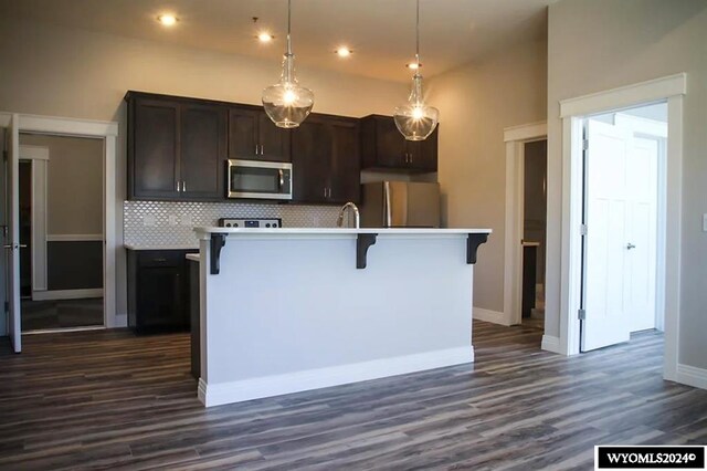 kitchen featuring dark brown cabinetry, tasteful backsplash, dark hardwood / wood-style flooring, a center island with sink, and refrigerator