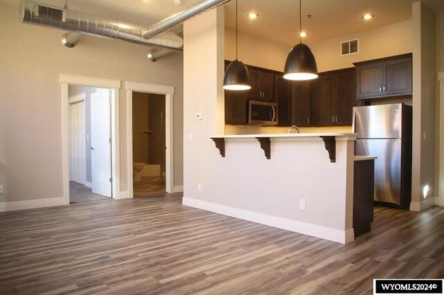 kitchen featuring a kitchen breakfast bar, pendant lighting, dark hardwood / wood-style floors, appliances with stainless steel finishes, and dark brown cabinetry