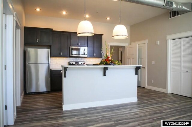kitchen with tasteful backsplash, dark hardwood / wood-style flooring, stainless steel appliances, and a center island with sink