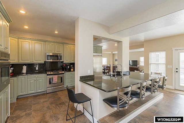 kitchen with appliances with stainless steel finishes, dark tile floors, backsplash, kitchen peninsula, and a kitchen breakfast bar