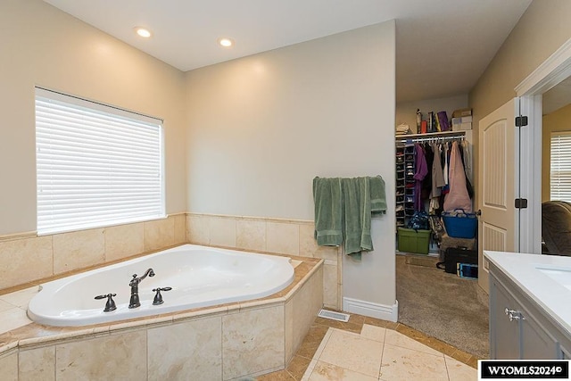 bathroom with a relaxing tiled bath, vanity, and tile floors